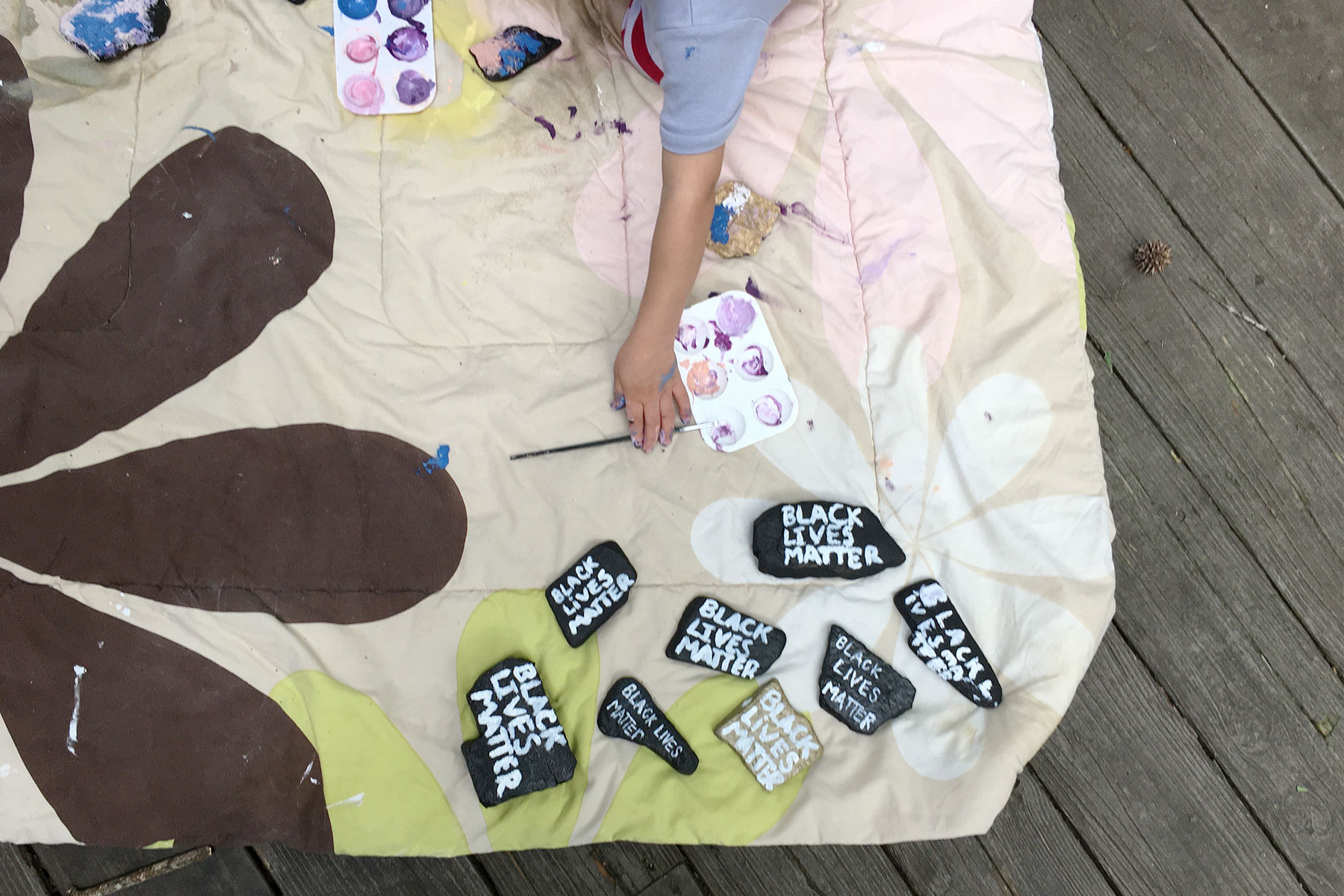 An image of a child painting "Black Lives Matter" on river rocks placed on a quilt.