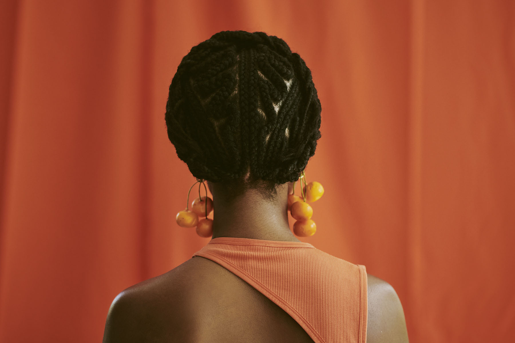 an unrecognized woman standing with braided hair with her back towards the camera.