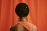 an unrecognized woman standing with braided hair with her back towards the camera.