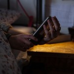 A teenager reaches for their phone at their bedside.