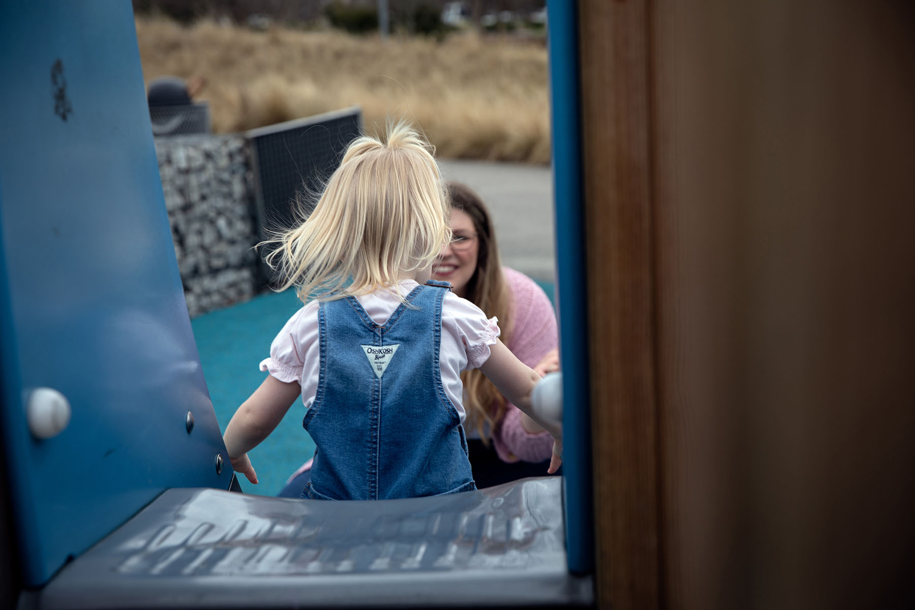 A small child is seen from the back as she plays with her mother at a playground.