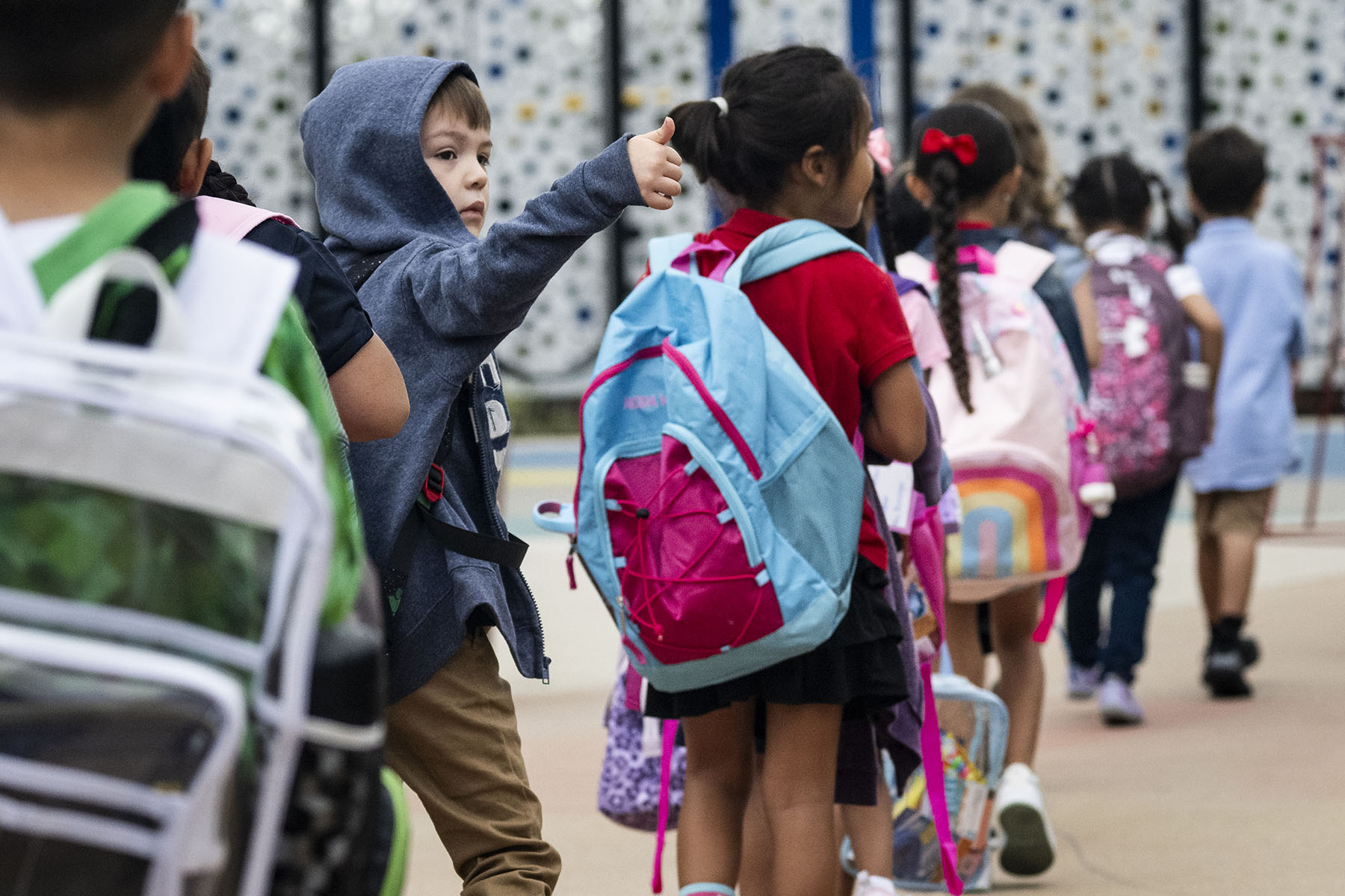 A kindergarten student gives a thumbs up to his parents as he heads to the first day of class.