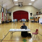 A poll worker wears a hijab as she sits at check-in table at Maples Elementary School.