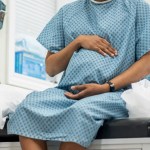 A young pregnant black woman sit up on an exam table in her doctors office during a routine prenatal check-up.