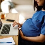 A pregnant woman works on a computer.