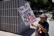 An advocate for cooling Texas prisons walks past a makeshift cell during a rally on the steps of the Texas Capitol. She is holding a sign that reads 