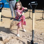 A girl holds a shovel with dirt.