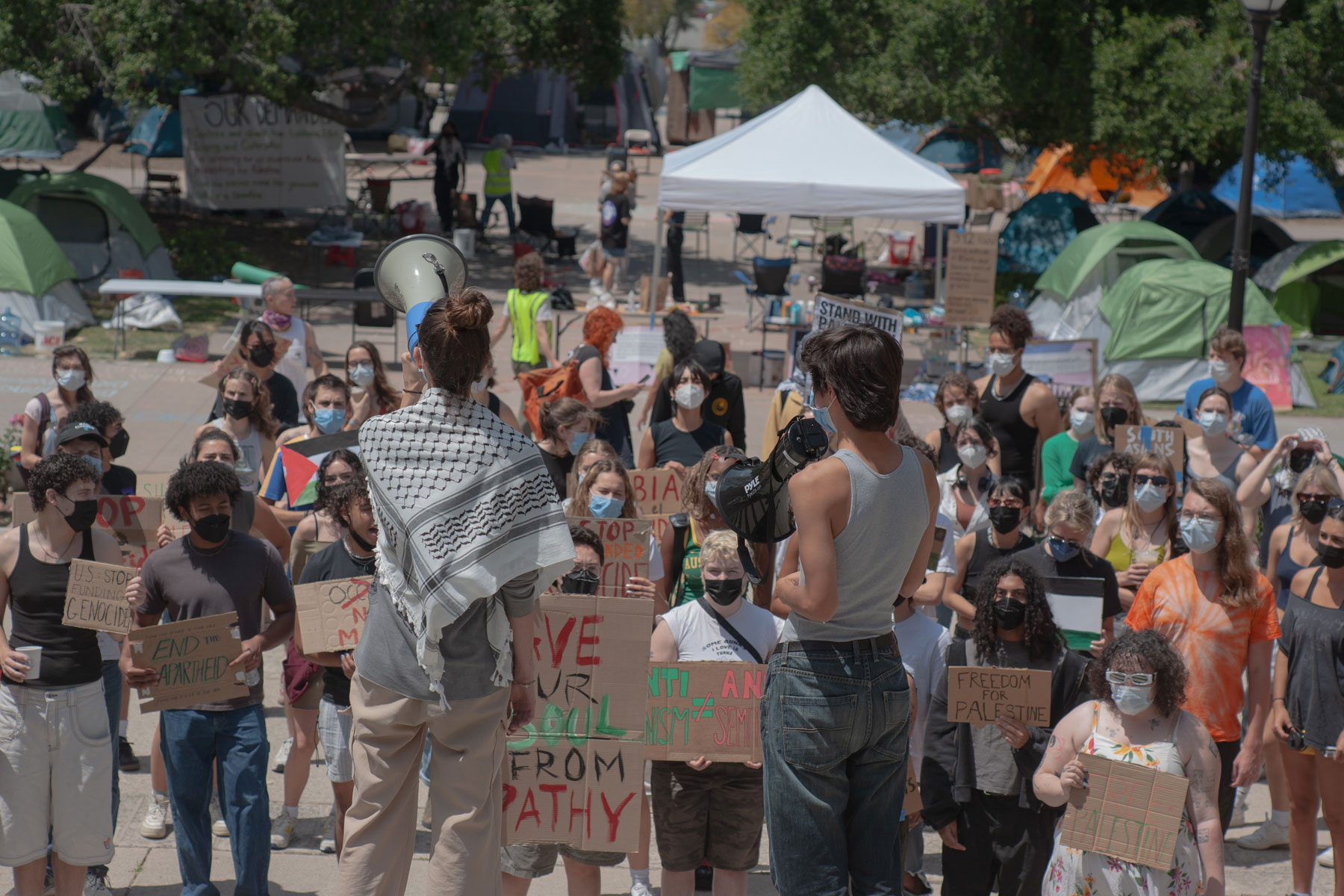 Two students (one draped in a kiffeh) and the other holding a bullhorn address student protestors at a pro Palestine protest at Occidental College.