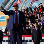 Donald Trump, wearing a suit and a re MAGA hat, points at a crowd at a rally in New Jersey