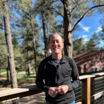 An image of Willy Chang Wilkinson on a deck at Camp Lost Boys. A cabin is in the background to his left.