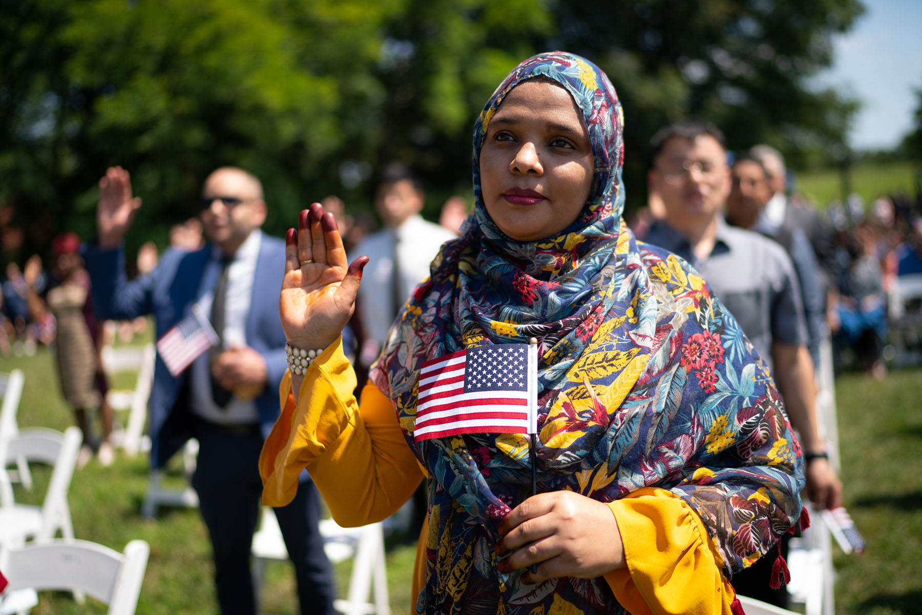 A woman raises her hand as she recites the pledge of allegiance during a naturalization ceremony at George Washington's Mount Vernon.