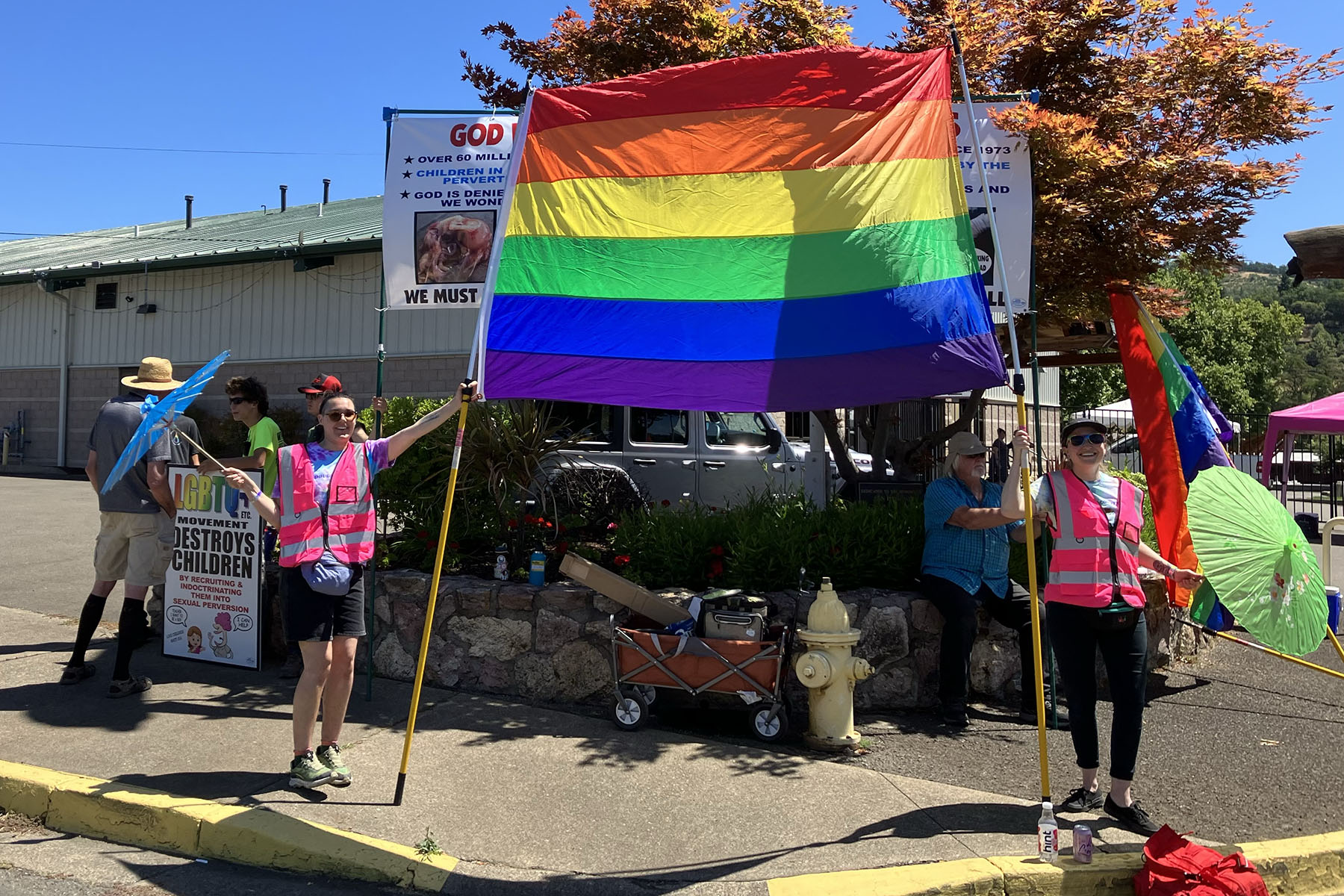 Frankie Leigh (right) and Skye Michelle hold a large pride flag in front of protesters.