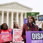 Ruth Glenn addresses a crowd during a rally in front of the Supreme Court as people hold signs behind her.