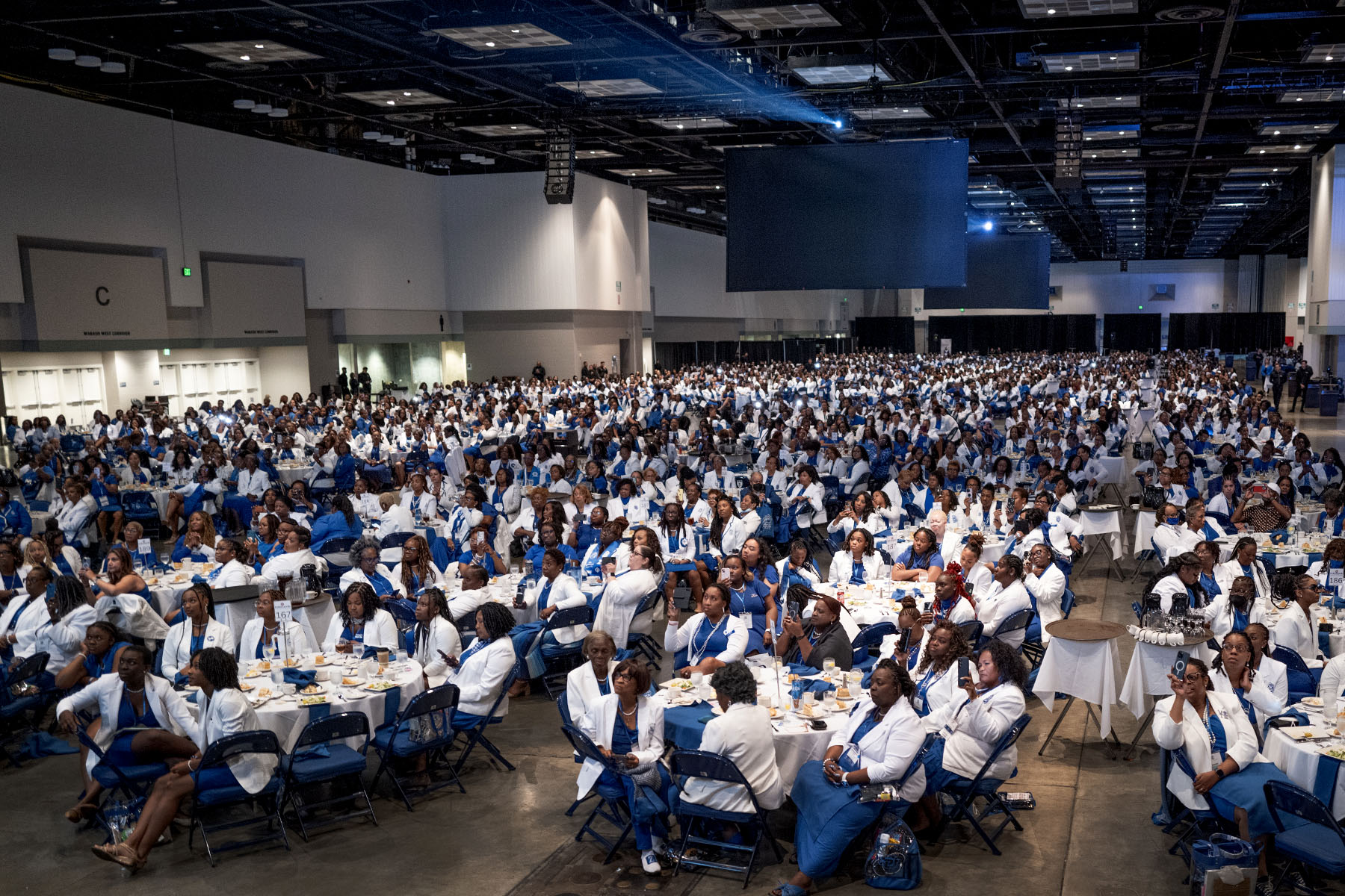 Guests dressed in blue and white fill tables as they listen to VP Harris speak at the Indiana Convention Center.