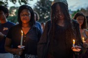 Two Black women close their eyes while holding candles during a candlelight vigil for Sonya Massey.