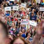 A large crowd of people attend a camapaign event for Vice President Kamala Harris. Several hold up signs that read 