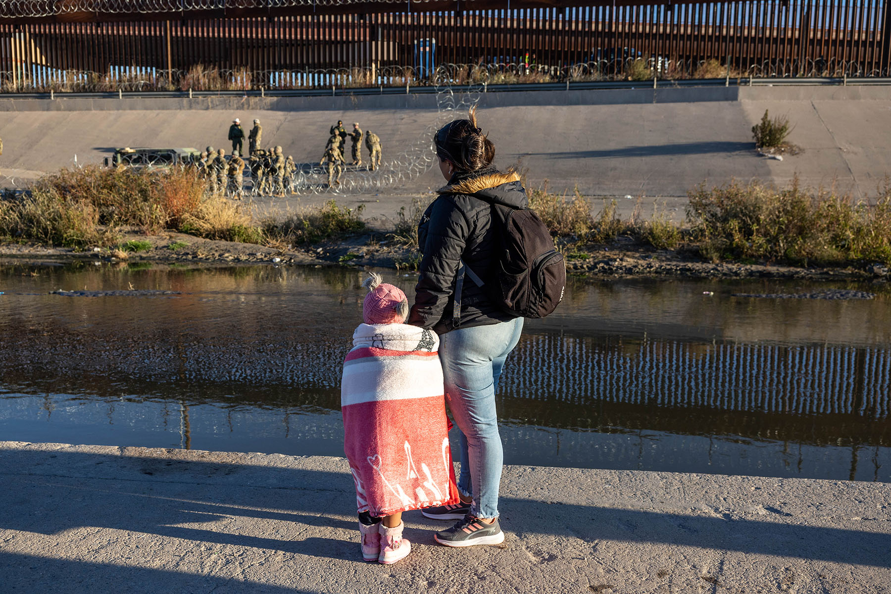 A mother and child look across the bank of the Rio Grande towards the U.S. Mexico border where Texas National Guard troops are posted.