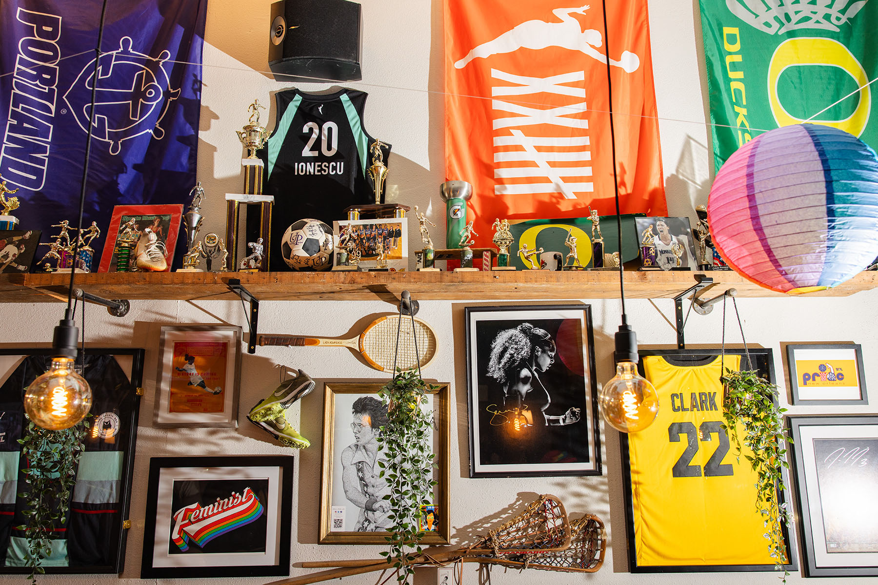 Memorabilia covers the walls at the Sports Bra including a Caitlin Clark jersey, a Ionescu jersey, assorted trophies, tennis rackets, a signed photo of Serena Williams and a drawing of Billie Jean King.