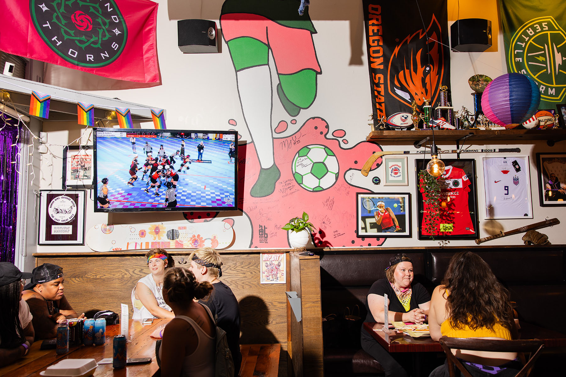 Patrons enjoy food and drink at The Bra as a roller derby game plays on a TV screen.