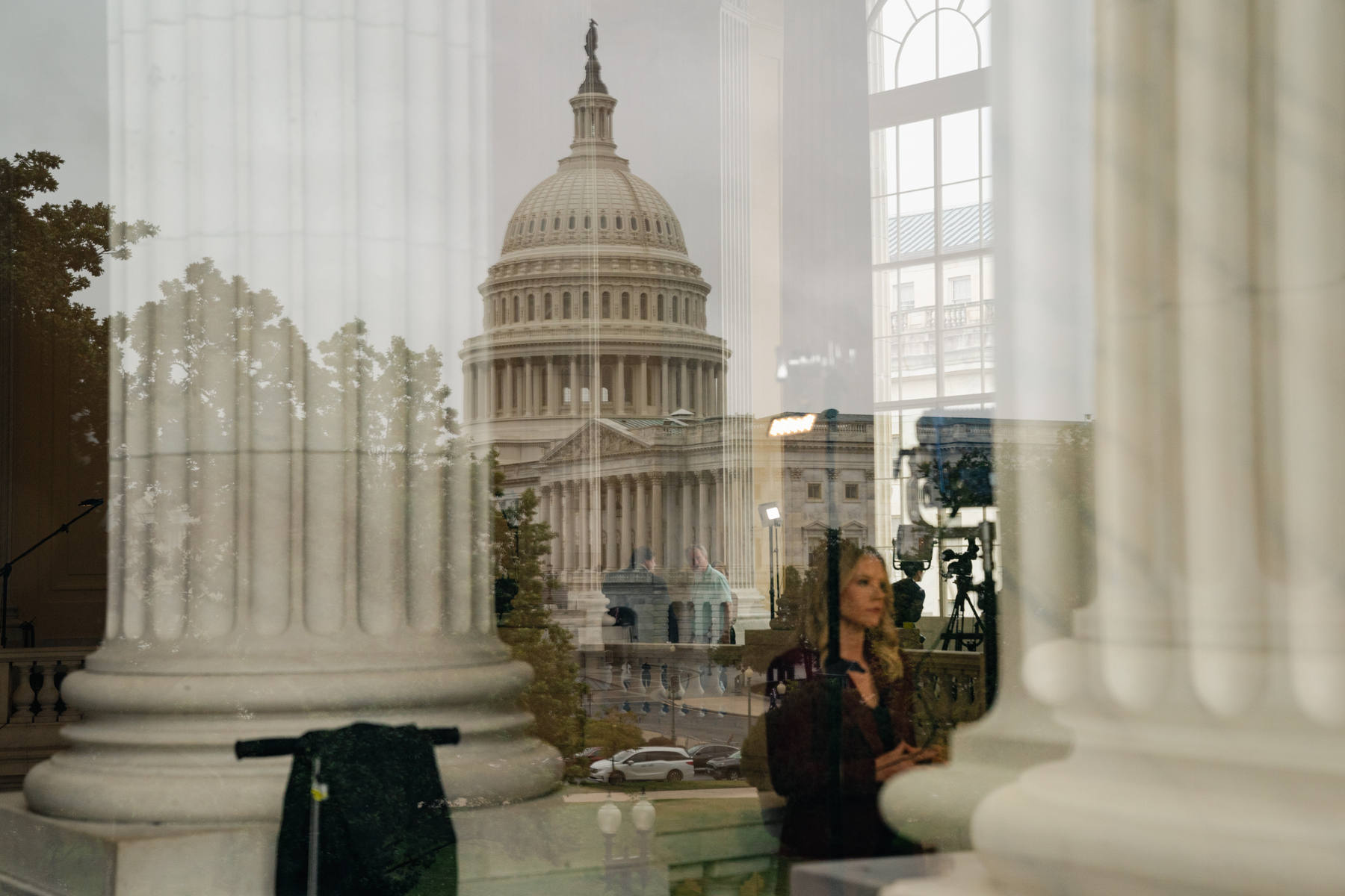 A woman stands near a column, with a reflection of the Capitol in the background.