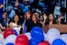 Vice President Kamala Harris is seen smiling and waving from a stage, surrounded by her family and extended family who are also waving and cheering.