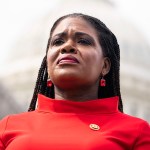 Close up of Cori Bush wearing a red dress with the Capitol dome in the background.