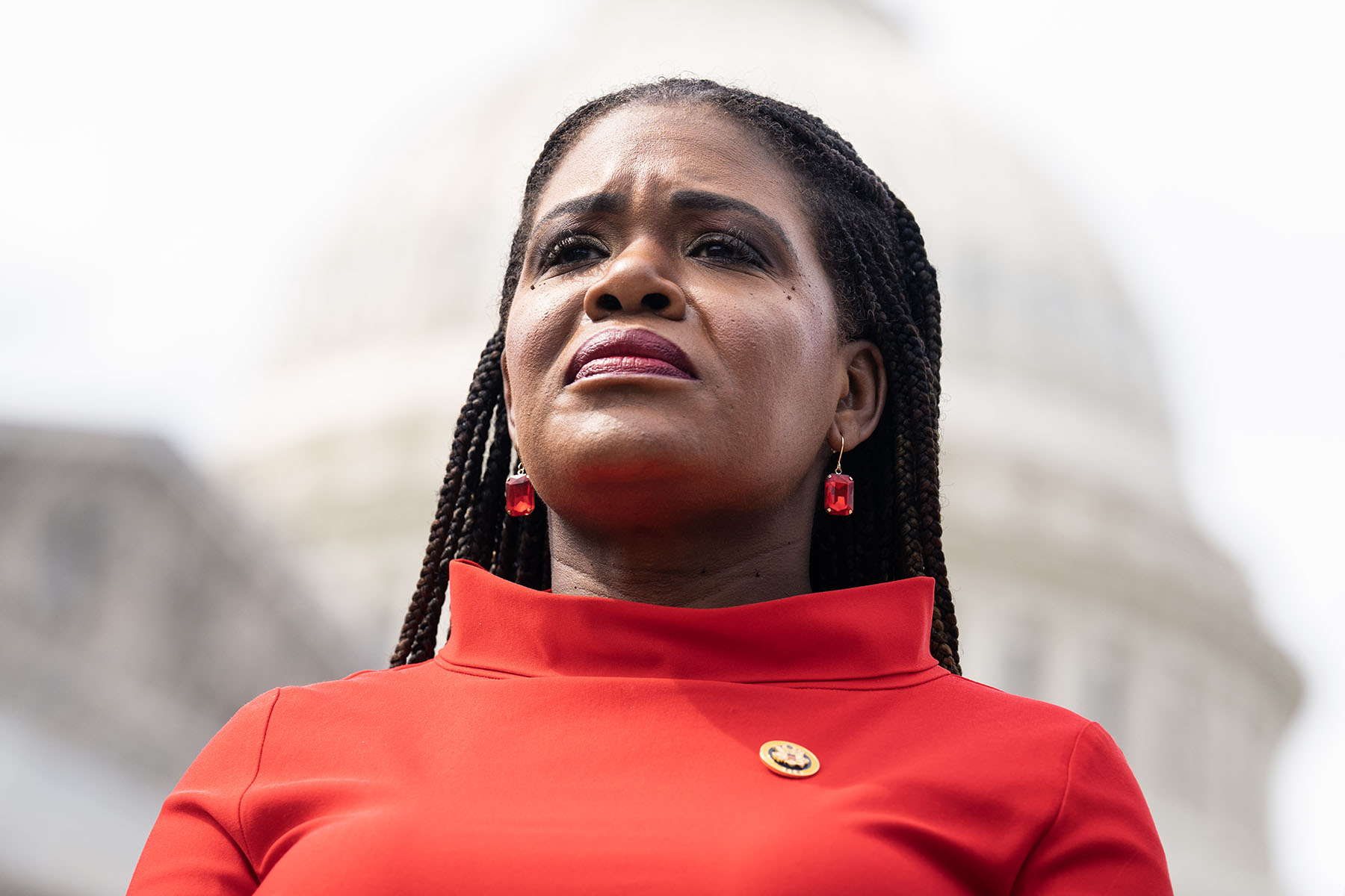 Close up of Cori Bush wearing a red dress with the Capitol dome in the background.