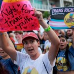 People protesting Florida Gov. Ron DeSantis and Florida lawmakers that passed anti-LGBTQ laws walk in the Stonewall Pride parade. In the foreground, a person holds a sign that reads 