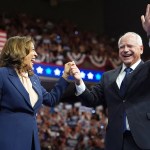 Vice President Kamala Harris and Gov. Tim Walz hold hands as they greet supporters from the stage.