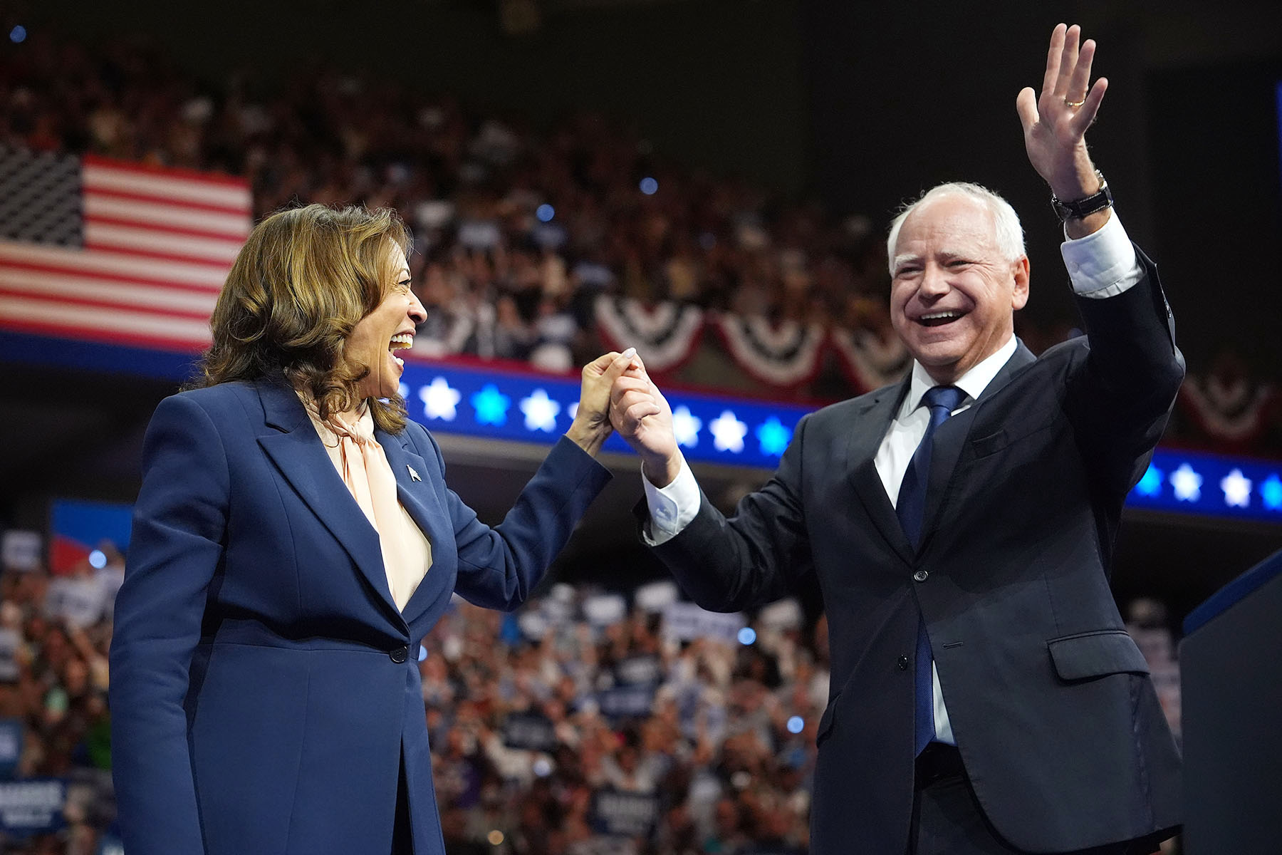 Vice President Kamala Harris and Gov. Tim Walz hold hands as they greet supporters from the stage.