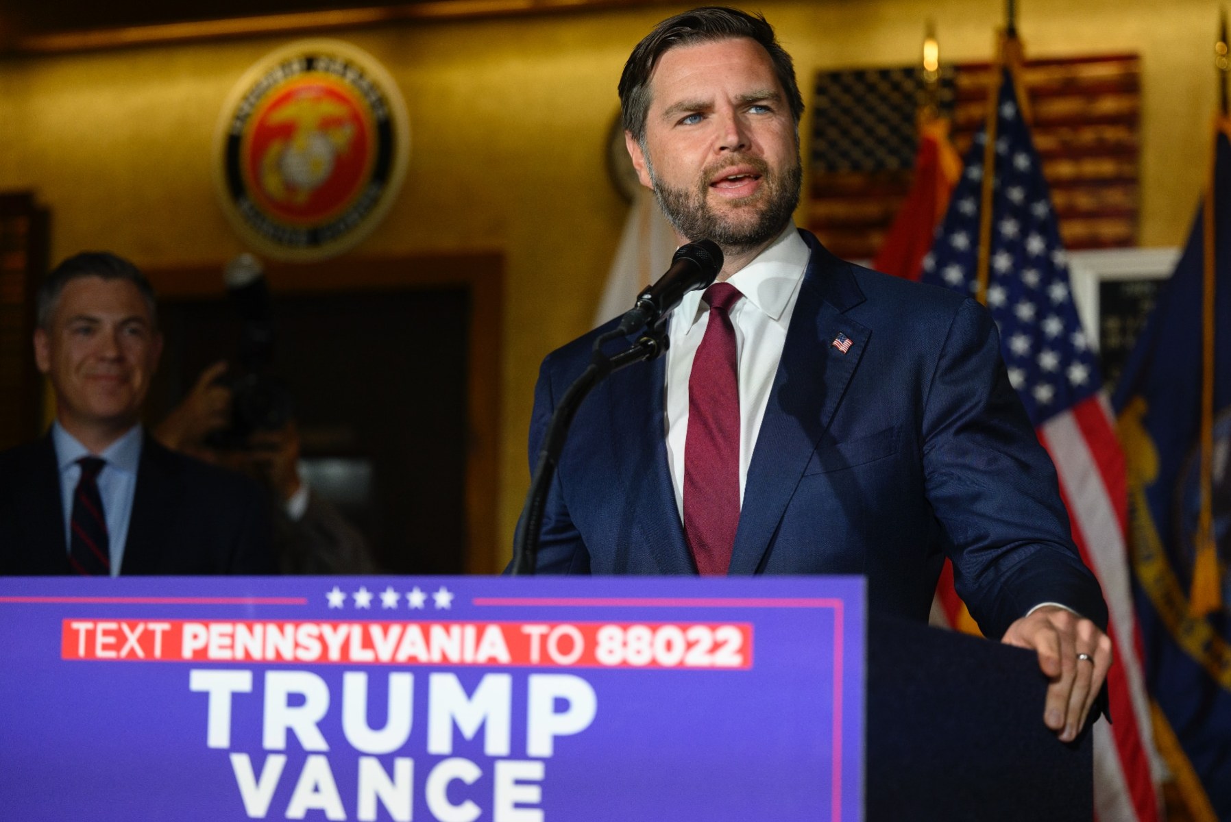 Sen. JD Vance stands behind a lectern with a Trump Vance sign