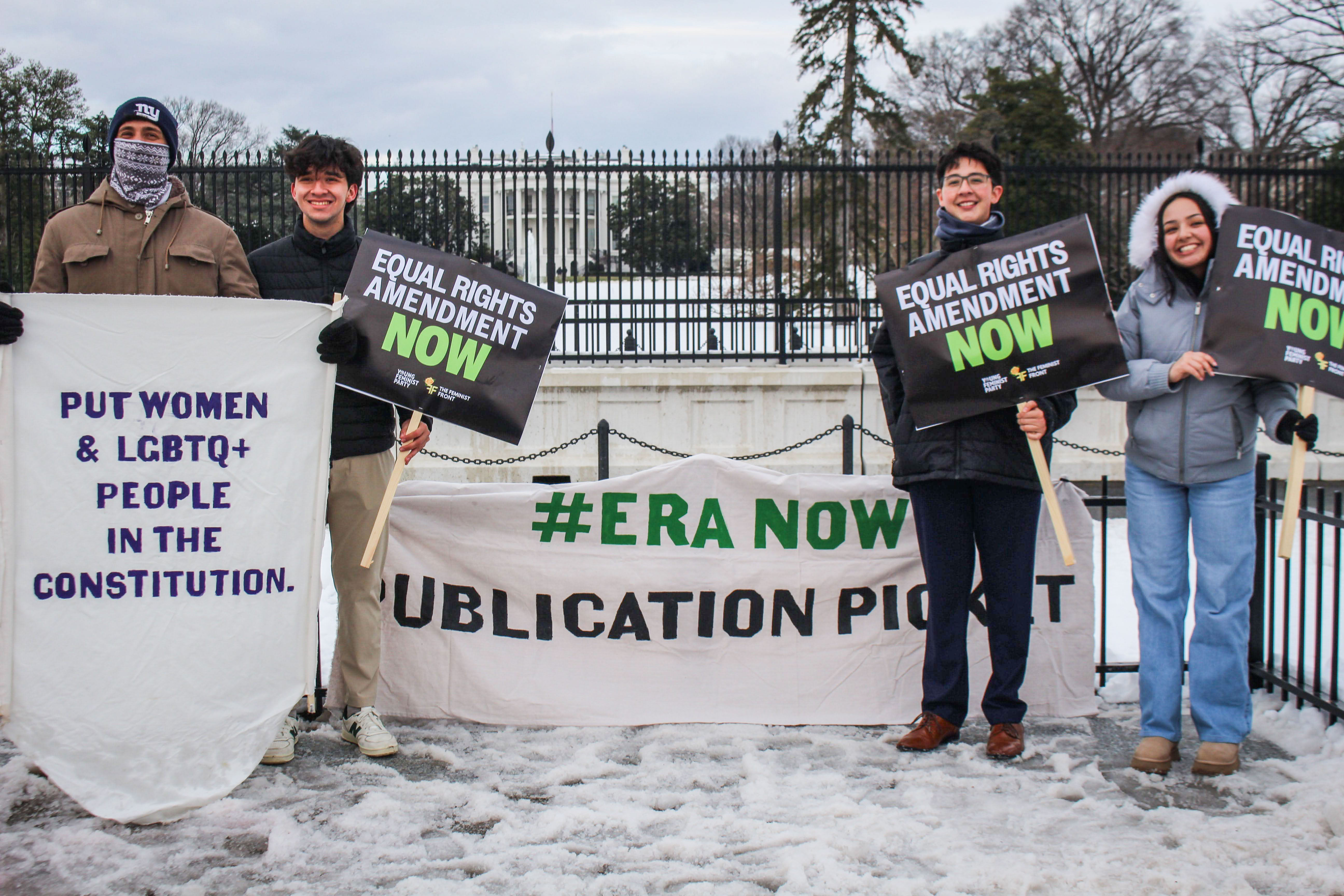 People standing in the snow outside the White House holding ERA Now signs.