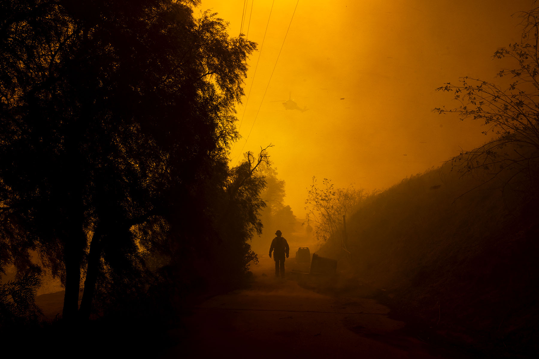 A firefighter walks on a path engulfed in smoke and embers as high winds push the Mountain Fire in Camarillo Heights, Camarillo, California.