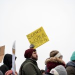 A line of protestors hold up signs saying 