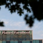 A Planned Parenthood building against a blue sky framed by shadows from tree leaves.