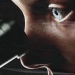 A person peers into a microscope. Their eye is intense and illuminated, framed by dark shadows and a distressed, plastic-like overlay.