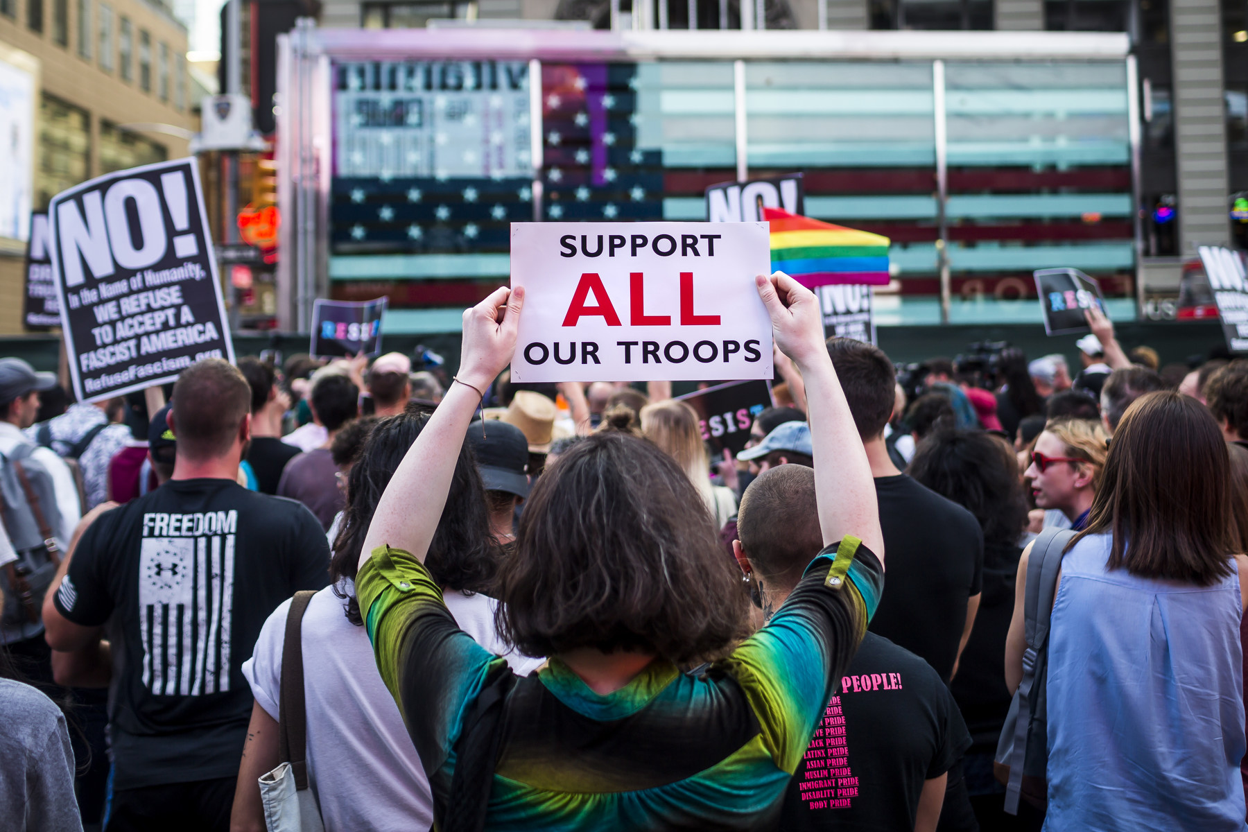 A person holds a sign saying "support ALL our troops"
