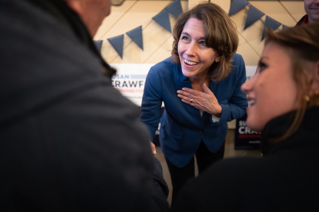 A woman smiles as she shakes hands with two people.