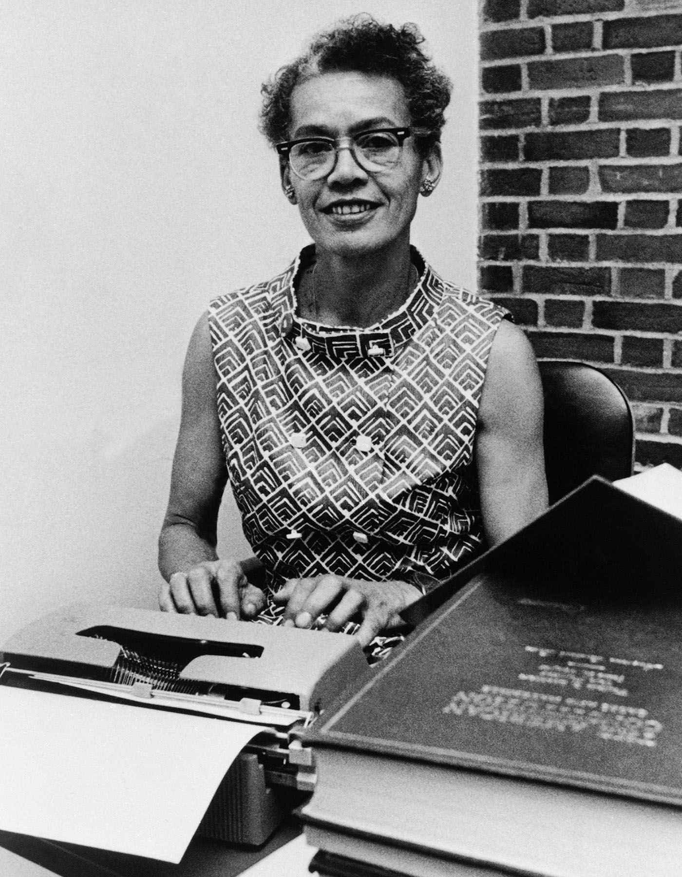 Brandeis professor Dr. Pauli Murray poses for a portrait at a desk while typing on a typewriter.