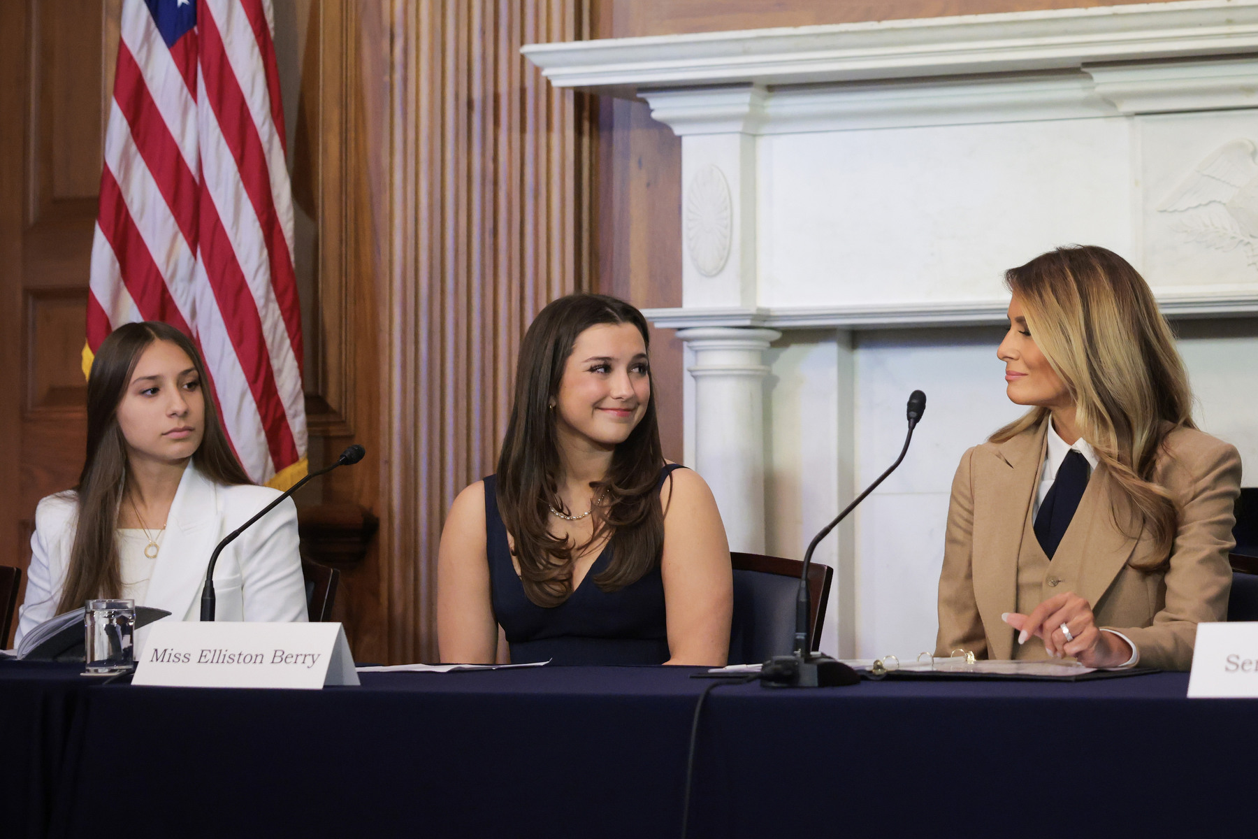 Three women look at each other while seated at a table.