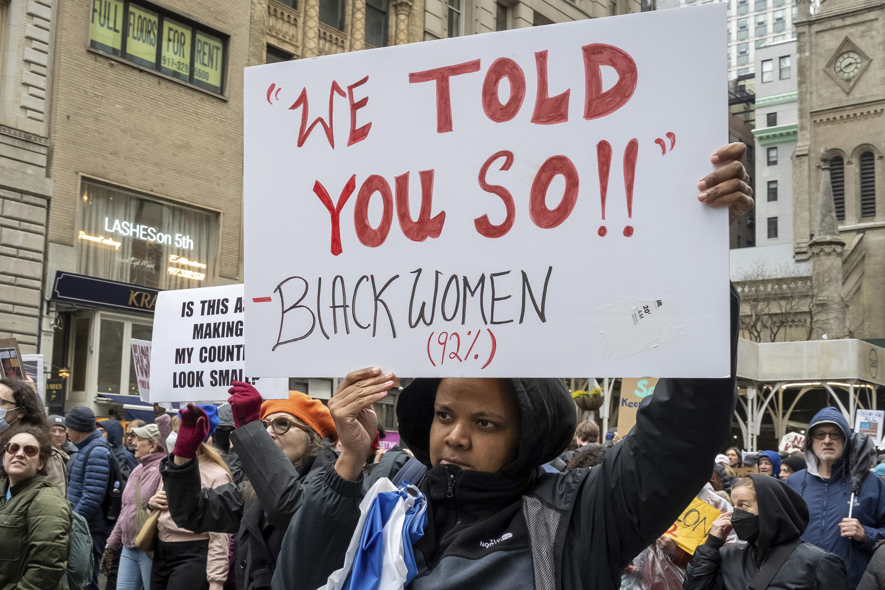 A Black woman holds a sign saying "we told you so"