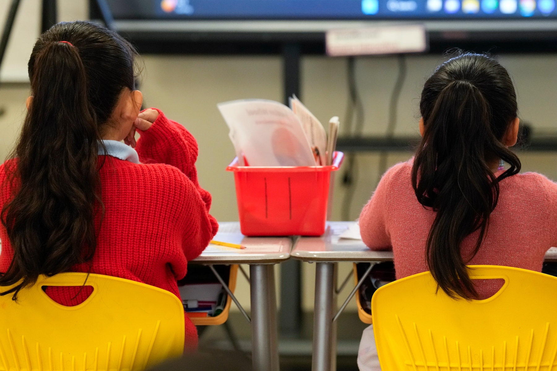 Two students sit facing a projector in a classroom.