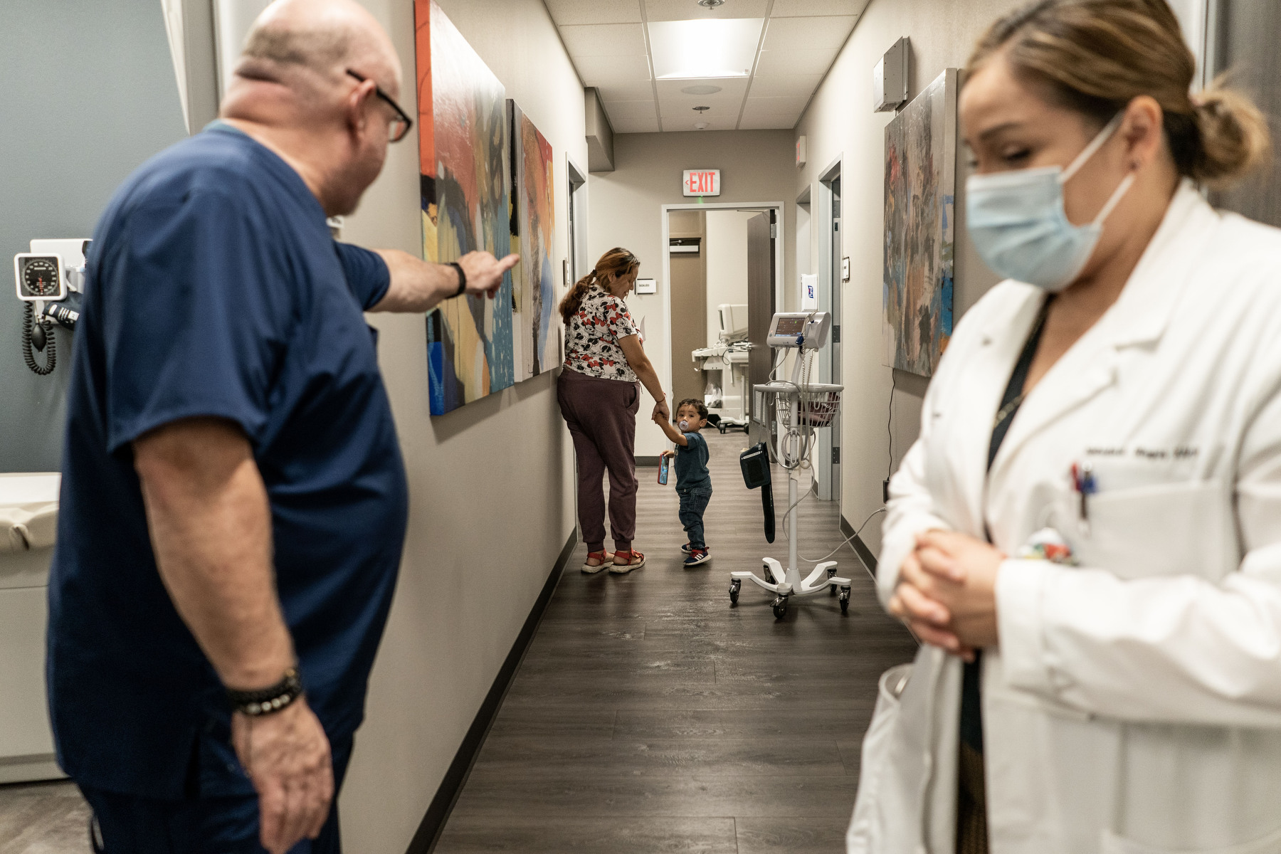 Medical workers wave goodbye to a mother and child patient in the hallway of a doctor's office.