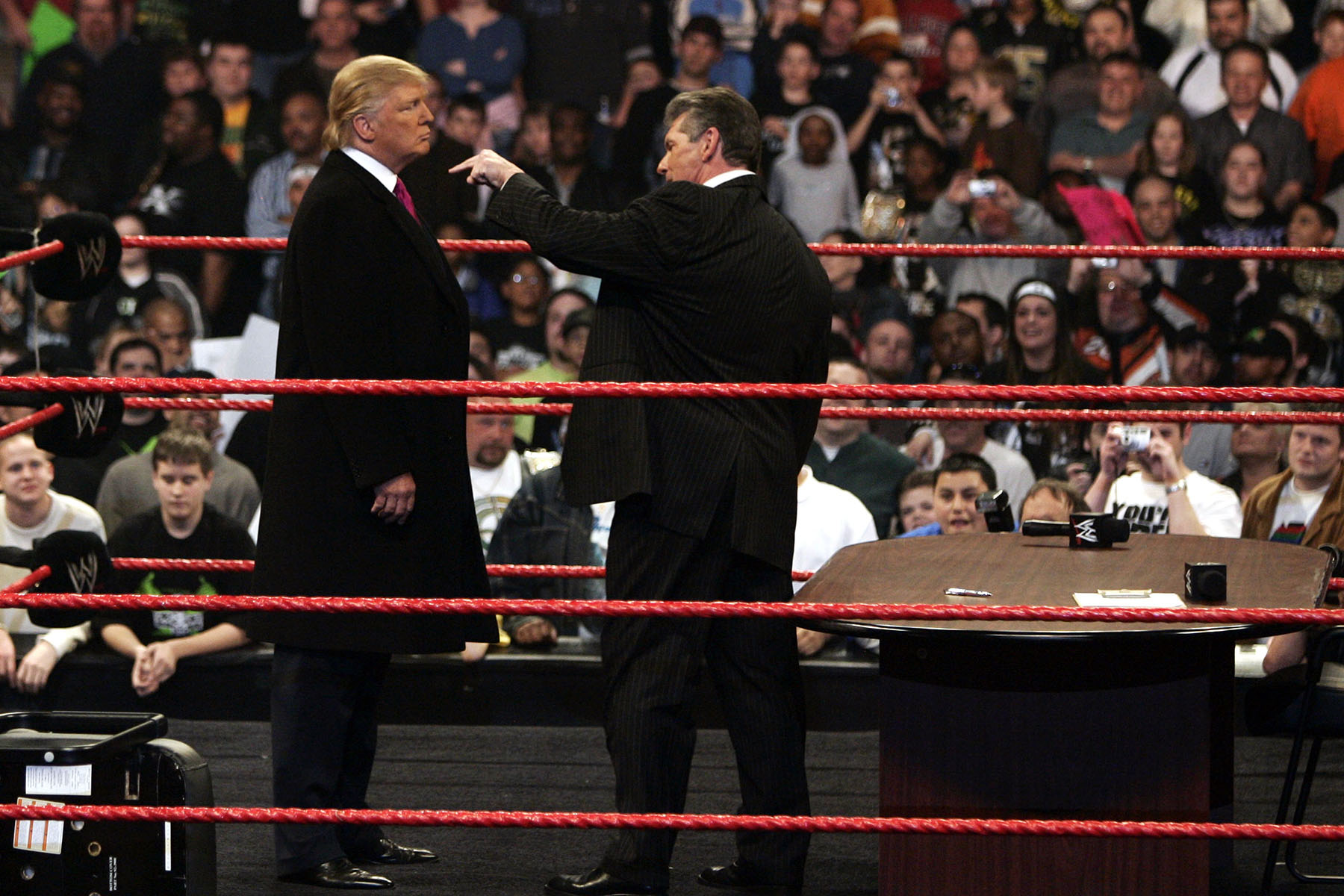 Donald Trump stands face to face with Vince McMahon in a wrestling ring as McMahon points at him during a WrestleMania contract signing event.