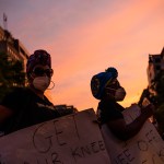 Black women protestors march in the streets against a sunset.