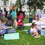 Mothers with young children sit on the grass outside the U.S. Capitol protesting cuts to Medicaid.