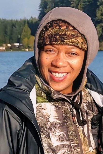 A woman smiles in front of a natural environment.