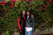 Mother and daughter stand in front of a wall of flowers.