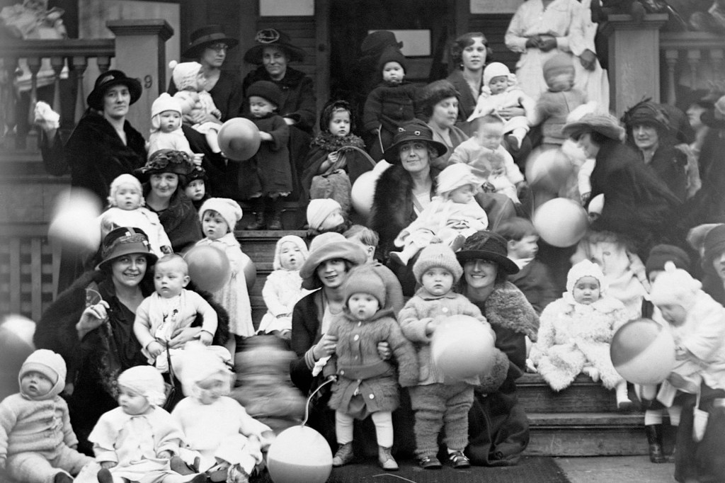 A historic black-and-white photo showing dozens of women and young children gathered on the steps of a large porch. Many children hold balloons.